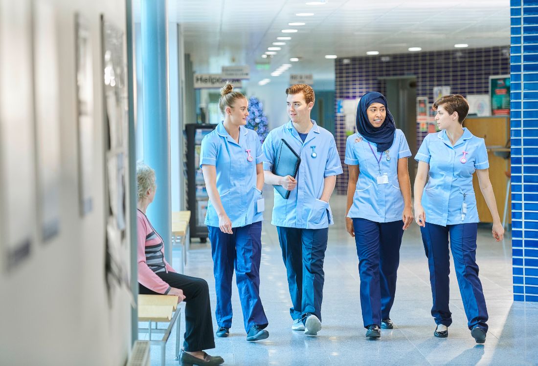 Four nurses walking down the corridor in a hospital protected by the risk of infection from using soluble laundry bags when transporting contaminated laundry.