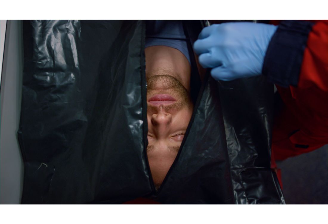 A medical professional puts a dead body in a dead body bag for proper storage.